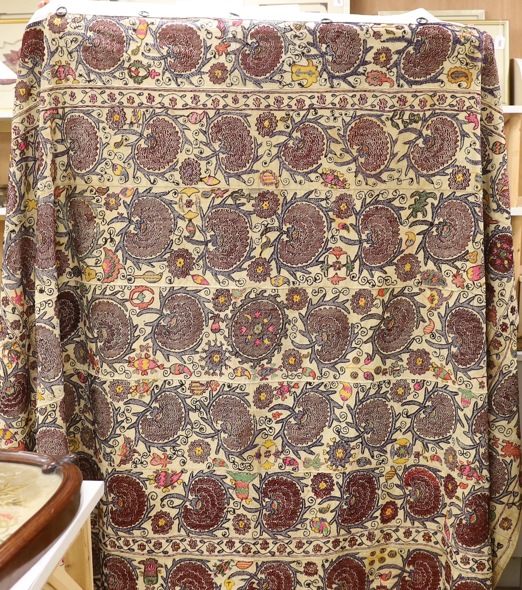 An exceptionally large Suzani hanging, embroidered with rows of stylised aubergine flower heads, the field filled with further polychrome flowers and serrated edged leaves, 190 x 270cm